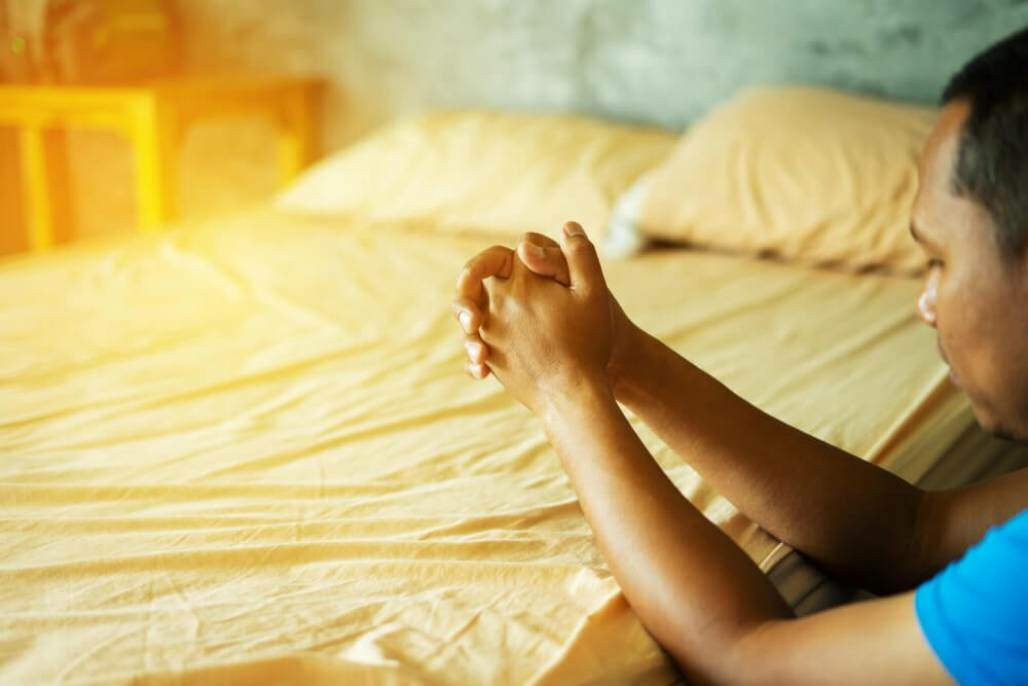 homem rezando ajoelhado ao lado da cama (Artit Fongfung AF/Shutterstock) homem rezando ajoelhado ao lado da cama (Artit Fongfung AF/Shutterstock)