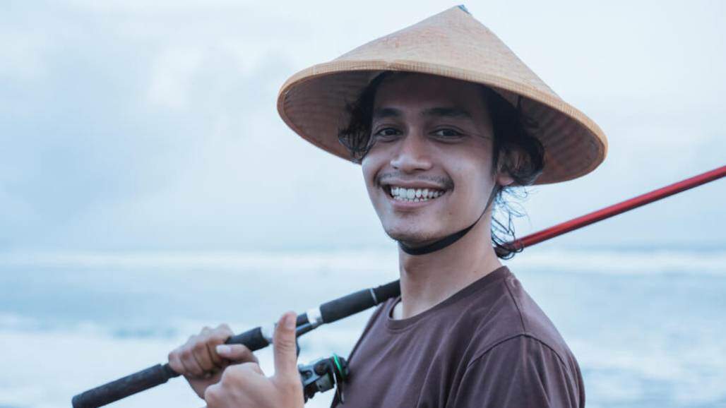 Jovem pescador sorrindo e com a vara de pescar em mãos (Shutterstock/ Odua Images) Jovem pescador sorrindo e com a vara de pescar em mãos (Shutterstock/ Odua Images)