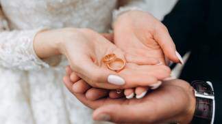 Noivo segura as mãos da noiva, onde estão dois anéis de casamento