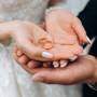 Noivo segura as mãos da noiva, onde estão dois anéis de casamento