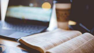 Captura aproximada de uma bíblia aberta com um laptop desfocado e um café