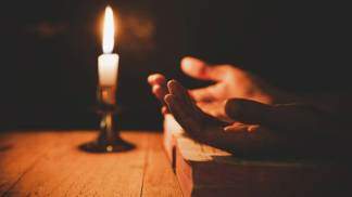 Mãos voltadas para cima em oração ao pai nosso com uma vela acesa ao fundo