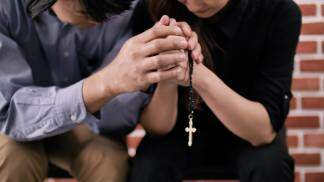 casal rezando o terço de mãos dadas