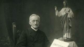 padre Dehon sentado ao lado da imagem do Sagrado Coração de Jesus