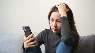 Mulher segurando o celular com a mão na cabeça com a expressão triste