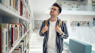moço de mochila em uma biblioteca escolhendo qual livro ler