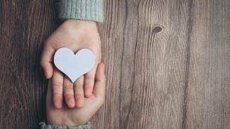 Duas mãos postas e um coração de papel no centro representando a gentileza