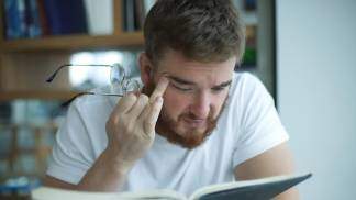 homem esfrega os olhos ao ler livro dificil