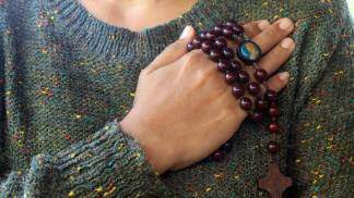 mulher com a mão no peito segurando um terço