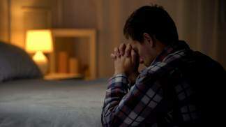 homem rezando ao pé da cama a noite