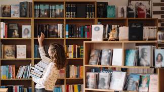 menina com livros na mão pegando mais livros na prateleira numa livraria