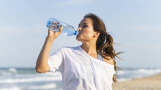 mulher-bebendo-agua-na-praia-