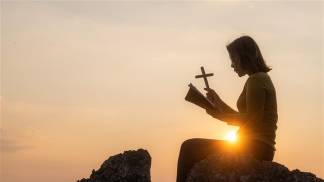 mulher rezando pôr do sol ao fundo