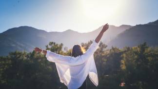 mulher com os braços abertos olhando para a montanha com uma expressão corporal de liberdade