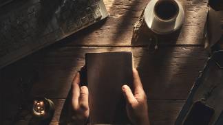 pessoa segurando a bíblia e rezando com um café e celular enquanto o sol nasce