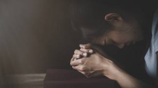 Mulher rezando com o rosto próximo das mãos