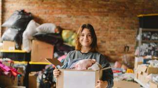 Mulher segurando um acaixa com roupas para serem doadas