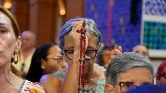 senhora ergue o terço na frente do rosto, de olhos fechados, rezando