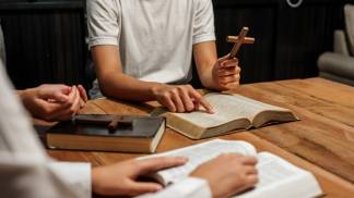 Uma mão segurando o crucifixo e outras mãos em estudo