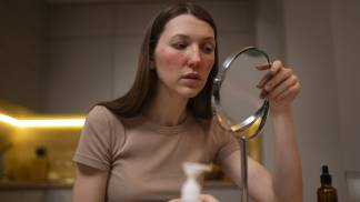 Mulher com a pele irritada se olha no espelho