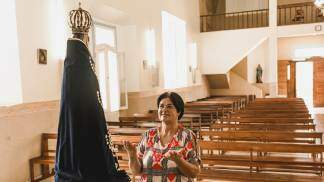 senhora rezando de frente para nossa senhora aparecida em uma igreja