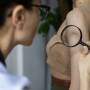 Médica analisando mancha na pele de uma mulher