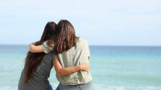 duas jovens amigas se abraçando olhando para o horizonte de frente para o mar