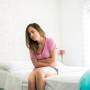 Mulher com as mãos no abdomen sentada na cama