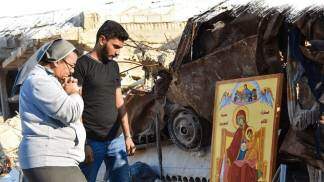 Duas pessoas rezando diante de um quadro de Nossa Senhora em meio a ruinas