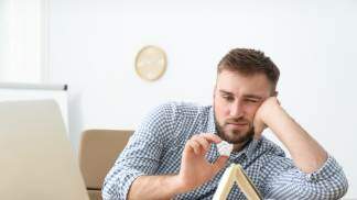 homem com preguiça sentado apoiando na mesa e jogando bolinha entediado 