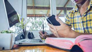 Um jovem menino fazendo seu estudo pelo celular com a Bíblia ao lado 