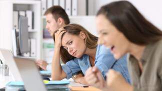 mulher com cabeça baixa na mesa olhando colega de trabalho feliz