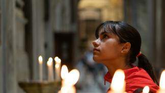 jovem na igreja olhando para cima fazendo oração perto de velas
